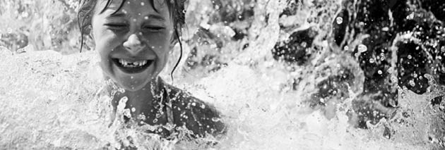 Little girl in waterpark pool being splashed by waterfall  Sunny summer day 